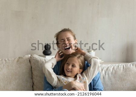 Cheerful giggling kid and young mom hugging, laughing, having fun. Mother holding in arms, cuddling, tickling cute daughter child on couch at home. Childcare, family, motherhood concept Foto d'archivio © 