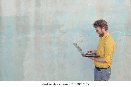 A Cheerful Ginger Hungarian Man With A Beard Using His Laptop Against A Wall