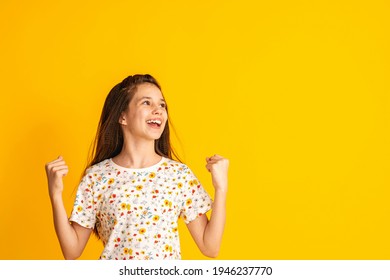 cheerful girl of about 10 years old in a floral T-shirt with her hands clenched into fists and a happy smile on a yellow background. A happy child enjoys success and victory. Discounts and sales - Powered by Shutterstock