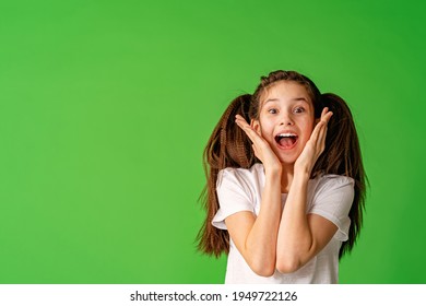 Cheerful Girl About 10 Years Old In White T-shirt Holding Her Hands Near Her Face And Happy Smile On Green Background. Happy Child Enjoys Success And Victory. Discounts And Sales. Advertising Concept
