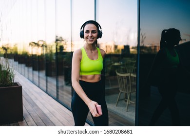 Cheerful Girl Athlete In Trendy Activewear Walking In Headphones Enjoying Active Healthy Lifestyle And Training, Happy 20s Caucasian Sports Woman Listening Music On Workout Use Accessory Outdoors