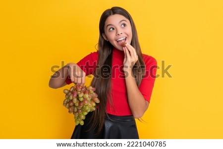 cheerful girl hold fresh grapes fruit on yellow background