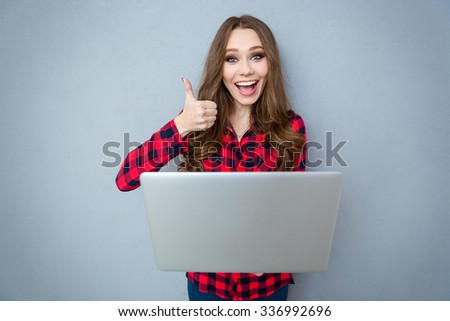 Cheerful girl holding laptop and showing thumb up