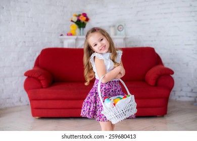 Cheerful Girl Holding A White Basket With Colorful Easter Eggs On Red Couch , The Child Laughs And Fun