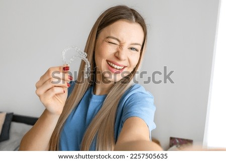 Cheerful girl make selfie holding an invisible braces aligner, recommending this new treatment. Dental healthcare concept.