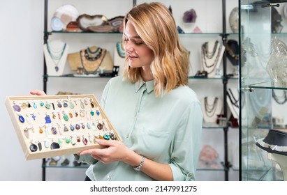 Cheerful girl showing pendants made of natural stones in jewerely shop