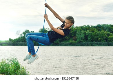 Cheerful Girl Swinging On A Rope Swing . Have A Fun Summer Vacation  Outdoor. Happy Child Have Fun On The Lake.