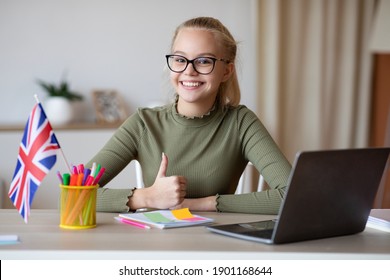 Cheerful girl teenager with flag of Great Britain showing thumb up, using laptop, having educational online course, studying english on Internet, home interior. English classes online concept - Shutterstock ID 1901168644