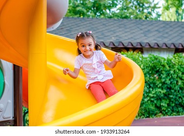 A cheerful girl with two pigtails on her head is riding a swing in the park and laughing. Emotional portrait of a child in the park