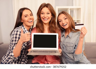 Cheerful girls showing laptop, bank card and gesturing