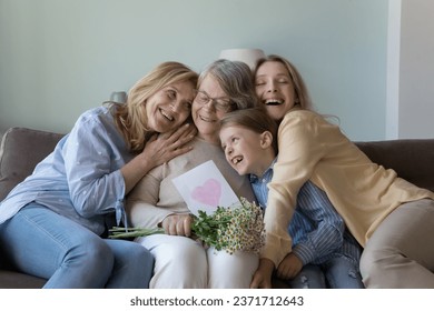 Cheerful girls and women congratulating eldest great grandma on birthday, giving flowers, hand drawn greeting card with heart from kid. Four female family generation hugging, celebrating mothers day - Powered by Shutterstock