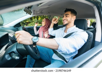 Cheerful Glad Young Arab Man Driving With Female In Hijab, Ride In Car, Couple Enjoy Music And Dance In Cabin On Journey. Fun In Road Trip, Vacation, Love, Relationship And Family Vacation, Copy Space