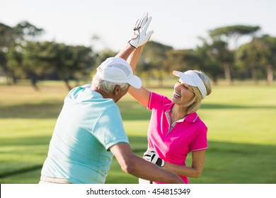 Cheerful golfer couple giving high five while standing on field - Powered by Shutterstock