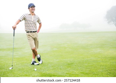 Cheerful golfer holding his club with hand on hip at the golf course