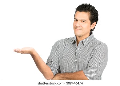 Cheerful, Good Looking Hispanic Male In Casual Button Down Dress Shirt Looking At Camera Grinning Holding Open Hand Out To Side Showcasing An Imaginary Product On His Flat Empty Palm. Horizontal