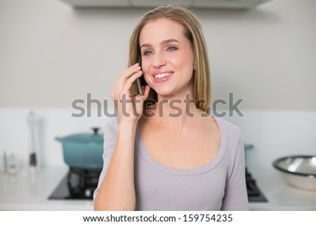 Cheerful gorgeous model phoning looking away standing in kitchen