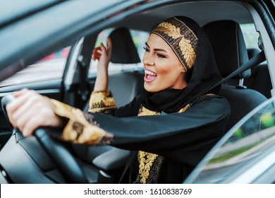 Cheerful Gorgeous Positive Muslim Woman In Traditional Wear Driving Her New Car, Listening Music And Singing.