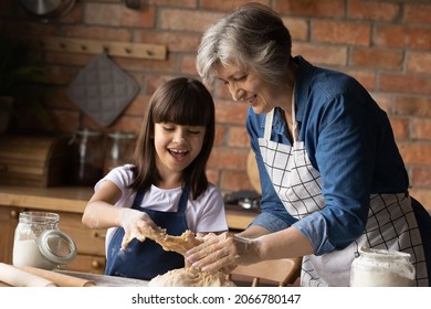 Cheerful Granddaughter Kid Helping Happy Grandma To Knead Dough, Cooking Pastry In Kitchen. Funny Girl With Flour On Face Helping Grandmother To Cook Dessert For Family Lunch, Dinner