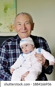 Cheerful Grandfather With Small Cute Baby Grandson Posing At Home Looking Ahead. Concept Of Two Generation Family. Everyday Joy Lifestyle Without Age Limitation.