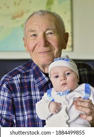 Cheerful Grandfather With Small Cute Baby Grandson Posing At Home Looking Ahead. Concept Of Two Generation Family. Everyday Joy Lifestyle Without Age Limitation.