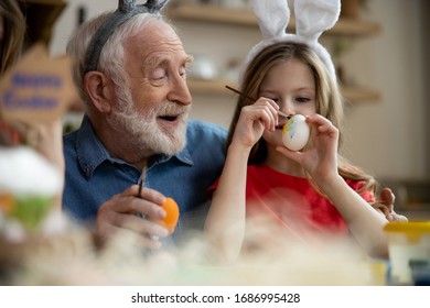 Cheerful Grandfather Smiling And Watching His Cute Granddaughter Painting Easter Egg