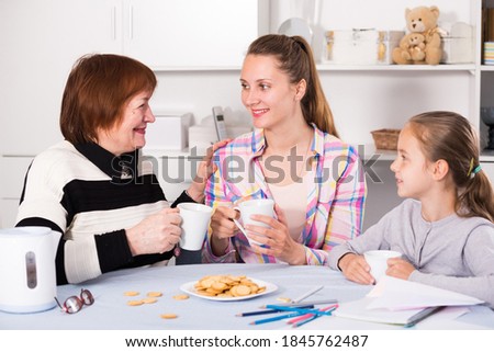 Cheerful grandmother, mother and grandchild drinking tea with cookies.