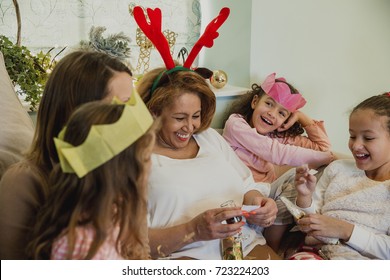 Cheerful Grandmother Is Reading A Joke From A Christmas Cracker To Her Granddaughters And Their Mum.