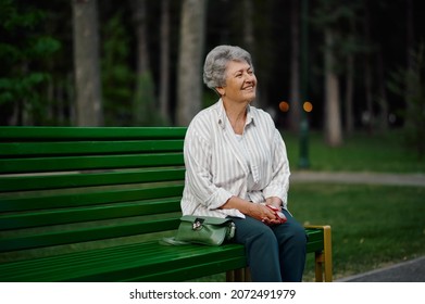 Cheerful granny leisures on bench in summer park