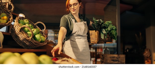 Cheerful Grocery Store Owner Restocking Fresh Produce In The Fruit And Vegetable Section Of Her Shop. Successful Female Entrepreneur Running A Small Business In The Food Industry.