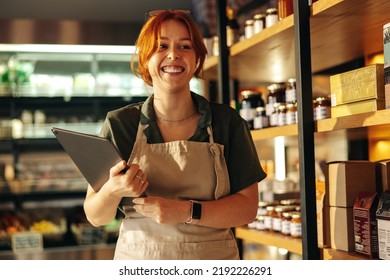 Cheerful Grocery Store Owner Smiling Happily While Holding A Digital Tablet. Young Female Entrepreneur Running A Successful Small Business In The Food Industry.