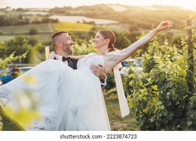 Cheerful groom carrying and spinning his bride while enjoying in vineyard on their wedding day.