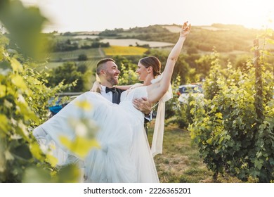 Cheerful groom carrying and spinning his bride while enjoying in vineyard on their wedding day.