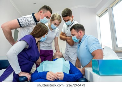 A Cheerful Group Of Dentists And Their Assistants Stand In The Dental Office And Smile Happily. The Concept Of Working Leisure For Physicians.