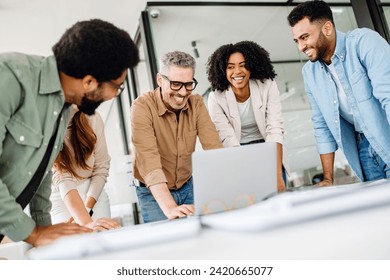 A cheerful group of diverse coworkers lean in around a laptop, indicative of an interactive tech discussion and the high spirits characteristic of a productive and forward-thinking team. - Powered by Shutterstock