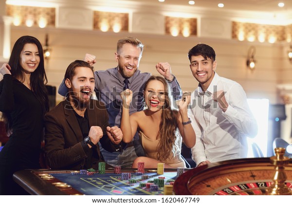 Cheerful group of friends at the table enjoys\
winning poker roulette in a\
casino.