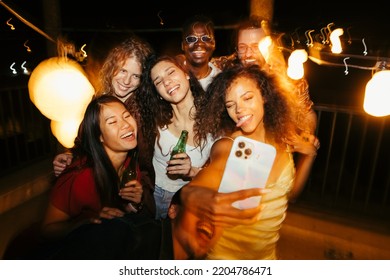 A cheerful group of friends are taking selfies at the rooftop party. They are smiling, making faces, and posing. Memories during summertime at the open-air club. - Powered by Shutterstock