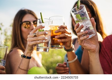 Cheerful group of millennial friends toasting alcoholic cocktails in the summer - people gathering cheering and drinking alcoholic drinks lifestyle concept