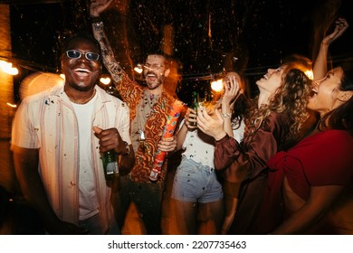 A cheerful group of people rejoices at the roof open-air nightclub and throws confetti. People are drinking, dancing and having a good time at the party.