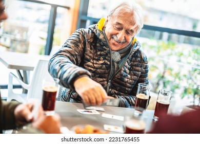 Cheerful group of seniors having fun playing card games at bar table - Old people enjoying free time together - Active retirement concept - Powered by Shutterstock