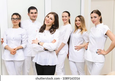 Cheerful Group Of Young Dentists And Their Assistants Standing In The Dental Office And Looking At Camera And Friendly Smiling At White Background Of Medical Room.