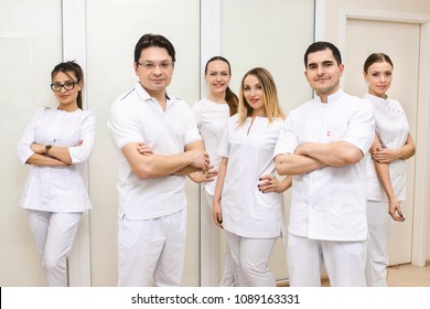 Cheerful Group Of Young Dentists And Their Assistants Standing In The Dental Office And Looking At Camera And Friendly Smiling At White Background Of Medical Room.