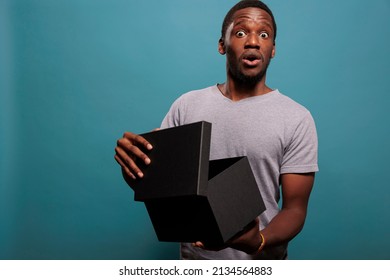 Cheerful Guy Feeling Surprised After Unpacking Gift Box And Opening To See Delivery Order. Shocked Man Unboxing Package Present From Postal Delivery Service, Enjoying Shopping Surprise.