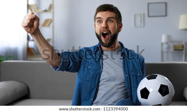 Cheerful guy loudly screaming watching football\
match, successful game\
result