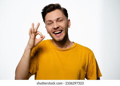 Cheerful Guy in a Yellow T-shirt Shows a Gesture of Okey on a White Background in the Studio. Positive Gesture, Ok Gesture. Copy Space. Close-up. High quality photo