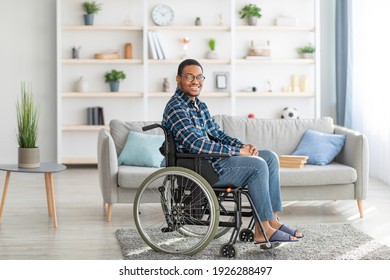 Cheerful Handicapped Black Guy In Wheelchair Smiling And Looking At Camera In Living Room. Portrait Of Positive Disabled Man Staying At Home, Feeling Happy And Optimistic