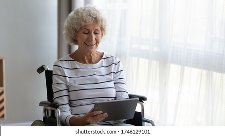 Cheerful handicapped elderly woman sitting in wheel chair holding tablet pad watch film at home, using on-line internet websites, modern services make life easier, get support online, have fun concept - Powered by Shutterstock