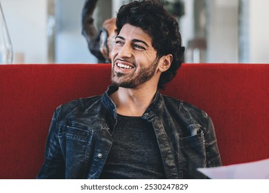 Cheerful handsome ethnic man sitting on red sofa in cafe holding laptop and printed picture and smiling away happy with result of work - Powered by Shutterstock