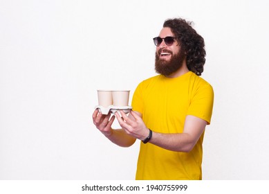 Cheerful Handsome Hipster Man With Long Hair Giving Someone Two Cups Of Coffee To Go.