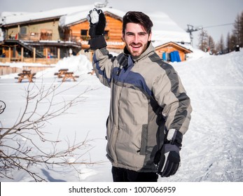 Cheerful Handsome Man In Outerwear Throwing Snowball Posing At Camera In Sunlight. 