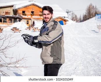 Cheerful Handsome Man In Outerwear Throwing Snowball Posing At Camera In Sunlight.